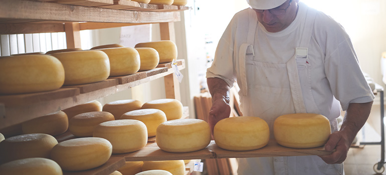 Man adding cheese wheels to a shelf